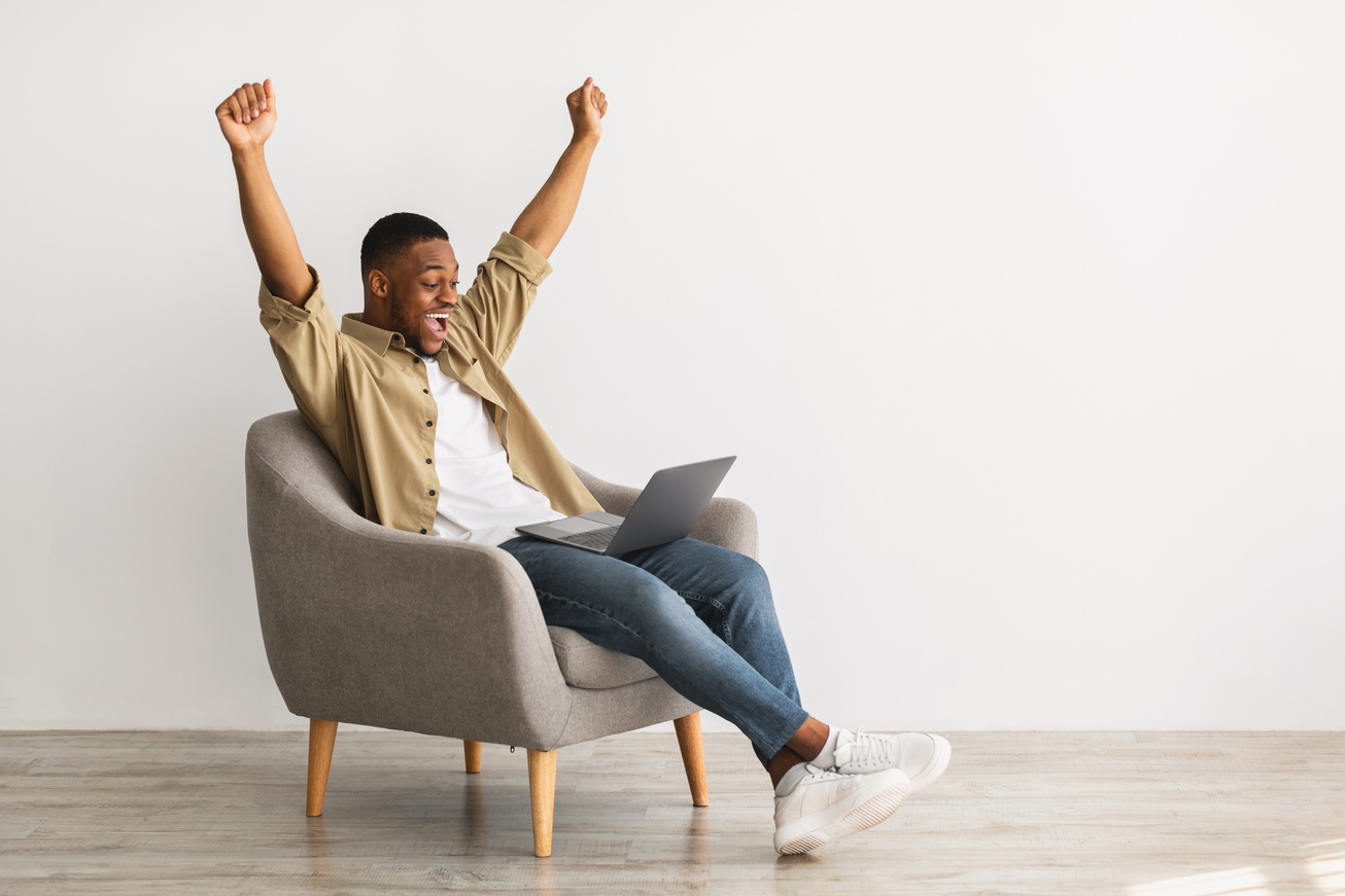 African Freelancer Man With Laptop Shaking Fists Over Gray Wall